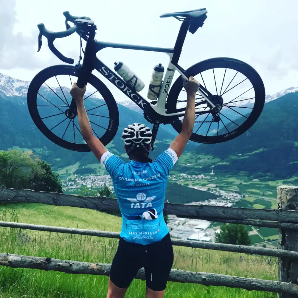 Radfahrerin hebt ihr Rad auf einem Bergpass über den Kopf
